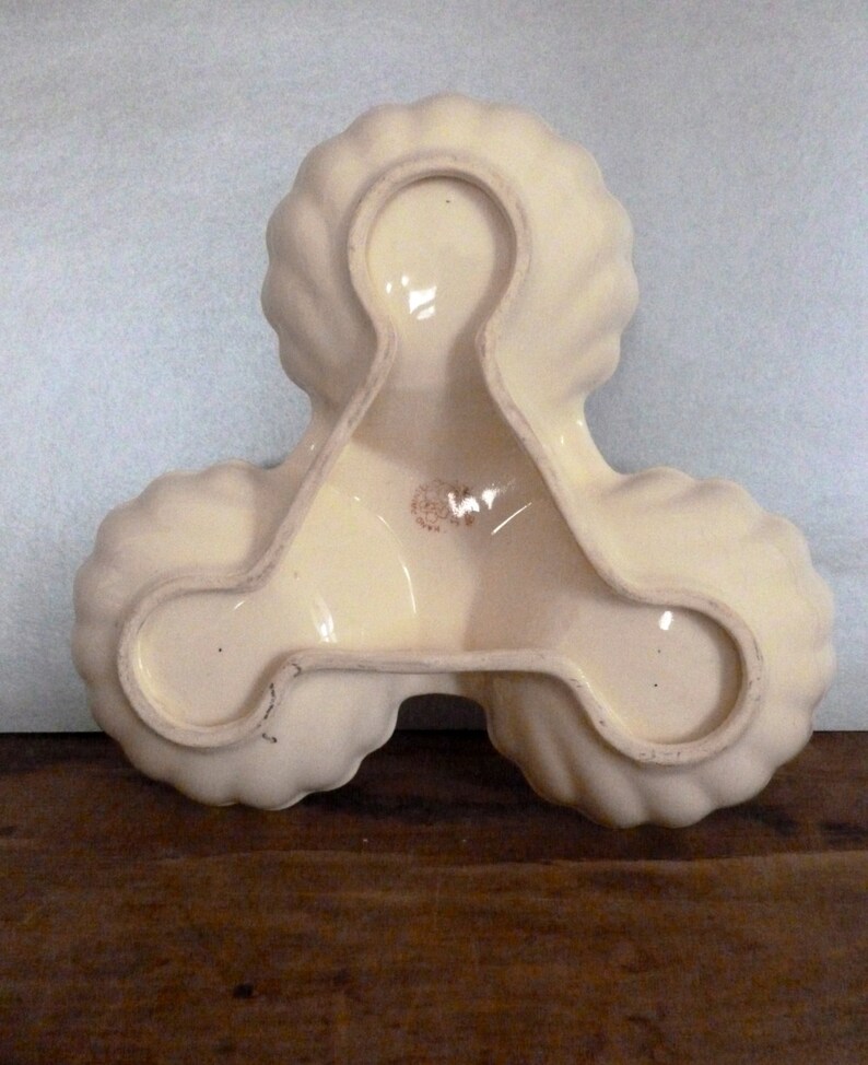 May include: A white ceramic serving dish with three sections, each shaped like a scallop shell. The dish is designed to hold three different types of food.