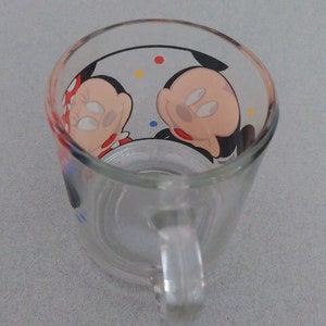 May include: A clear glass mug with a handle. The mug has a colorful design featuring Mickey Mouse and Minnie Mouse.