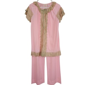 May include: A vintage pink pajama set with a short-sleeved top and wide-leg pants. The top features a ruffled neckline and lace trim in a contrasting beige color. The set is hanging on a white hanger.