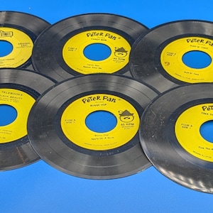 Puede incluir: Una colección de siete discos de vinilo negros con etiquetas amarillas. Los discos presentan a los personajes Peter Pan y Campanilla. Los discos se titulan "Peter Pan" y "Telephone Black Beauty".