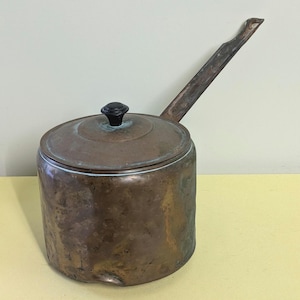 May include: Antique copper pot with a lid and a long handle. The pot has a dark brown wooden knob on the lid.