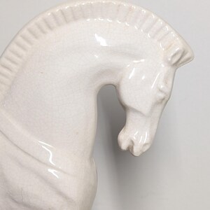 Puede incluir: Figura de caballo de cer&aacute;mica color crema. El caballo se representa de perfil, con la cabeza y el cuello arqueados. La figura tiene un acabado brillante y detalles de craquelado visibles, agregando textura. Un art&iacute;culo decorativo.