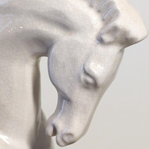 Puede incluir: Escultura de caballo de cer&aacute;mica gris claro. La cabeza del caballo est&aacute; inclinada hacia abajo, mostrando detalles y la superficie texturizada de la cer&aacute;mica. La escultura tiene un acabado craquelado.