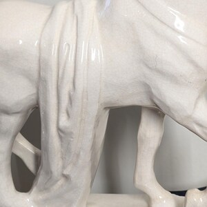 Puede incluir: Estatua de caballo de cer&aacute;mica blanquecina detallada. La escultura presenta una tela drapeada sobre el lomo del caballo y un acabado texturizado y agrietado. El caballo est&aacute; de pie.