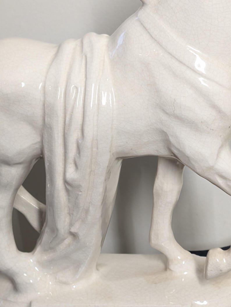 Puede incluir: Estatua de caballo de cer&aacute;mica blanquecina detallada. La escultura presenta una tela drapeada sobre el lomo del caballo y un acabado texturizado y agrietado. El caballo est&aacute; de pie.