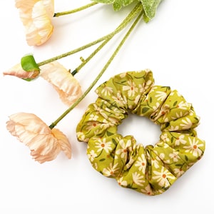 A handmade scrunchie showcasing shades of moss green, earthy browns, and pops of warm peach and blush pink.