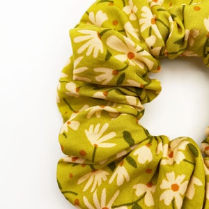 A handmade scrunchie showcasing shades of moss green, earthy browns, and pops of warm peach and blush pink.