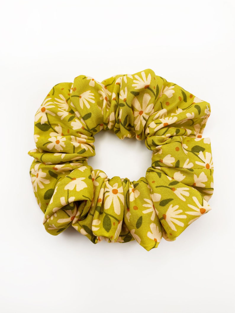 A handmade scrunchie showcasing shades of moss green, earthy browns, and pops of warm peach and blush pink.