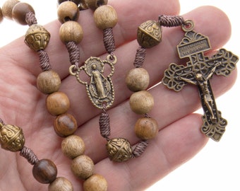 May include: A brown wooden rosary with a brass crucifix and a medal of the Virgin Mary. The rosary beads are strung on a brown cord.