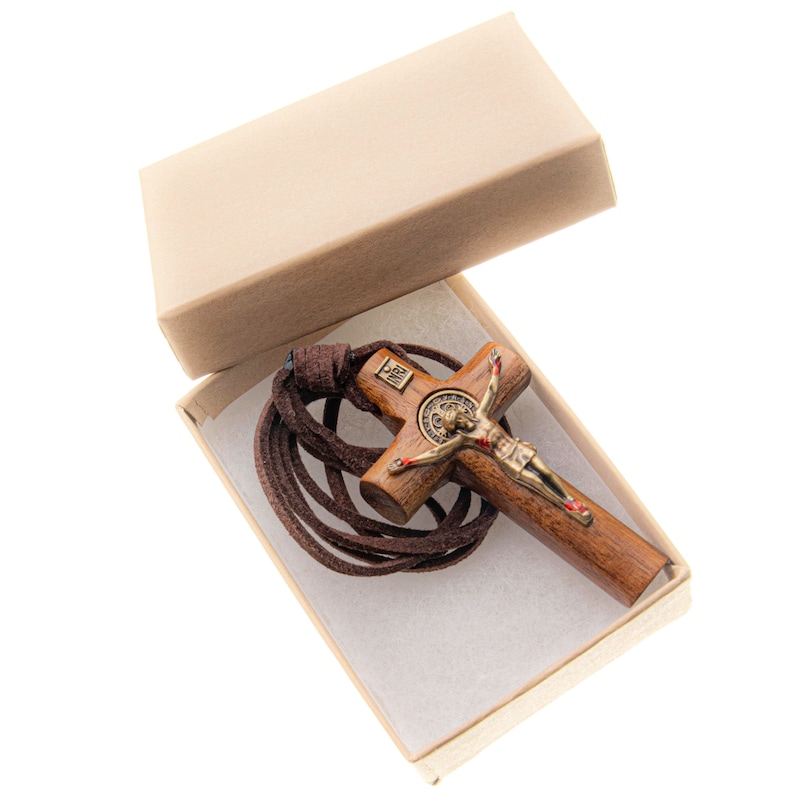 Pode incluir: Um crucifixo de madeira marrom com uma figura de Jesus de metal e um cord&atilde;o de couro marrom. O crucifixo est&aacute; em uma caixa de papel&atilde;o marrom com papel de seda branco.