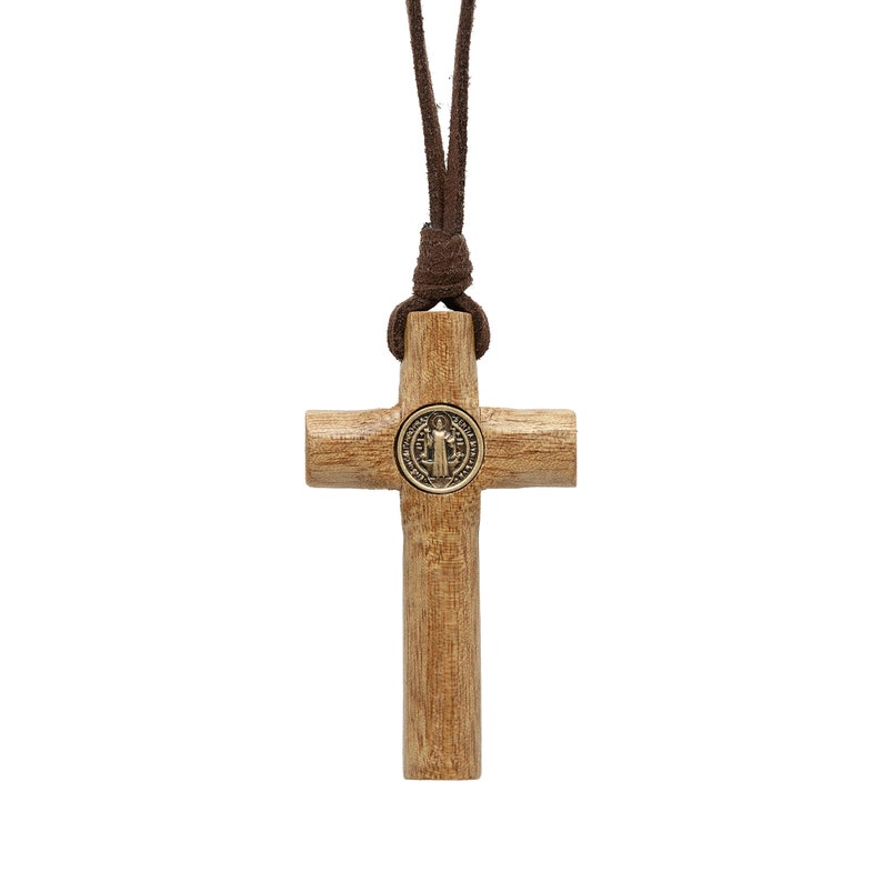 Pode incluir: Um colar com uma cruz de madeira e um cord&atilde;o de couro marrom. A cruz tem um pequeno medalh&atilde;o de metal no centro.