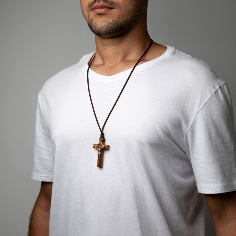 Pode incluir: Um colar de cord&atilde;o de couro marrom com um pingente de crucifixo de madeira. O crucifixo apresenta uma figura de Jesus dourada.