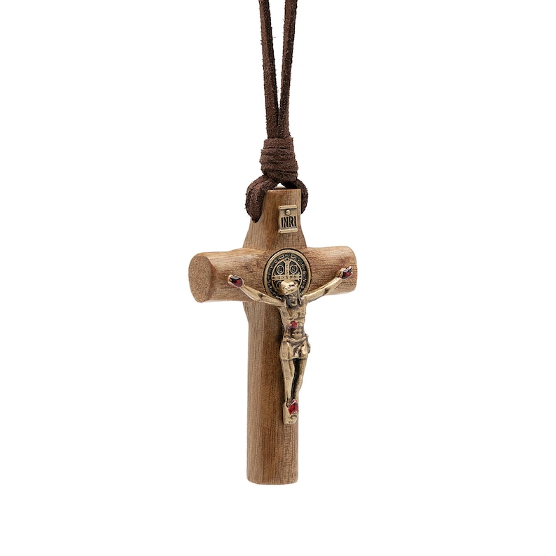 Pode incluir: Um colar com um crucifixo de madeira e um cord&atilde;o de couro castanho. O crucifixo apresenta uma figura de Jesus dourada com acentos vermelhos e uma medalha de S&atilde;o Bento.