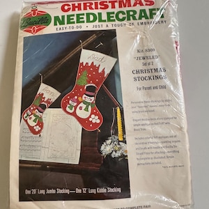 May include: A Bucilla Christmas Needlecraft kit 8309 for two jeweled Christmas stockings. The package features a red felt stocking design with snowmen, sequins, and beads. It includes one 20-inch jumbo stocking and one 12-inch kiddie stocking.
