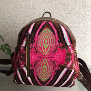 Könnte beinhalten: Ein brauner und pinkfarbener Rucksack mit einer Reißverschlusstasche vorne. Der Rucksack hat einen braunen Lederbesatz und verstellbare Träger.
