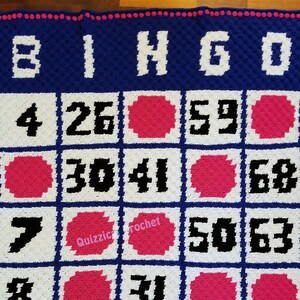 May include: A blue and white crochet bingo card with pink circles and black numbers. The numbers on the card are 4, 26, 59, 30, 41, 68, 7, 50, 63, 8, 31, 18, 24, 52.