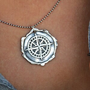 May include: A silver necklace with a compass pendant. The compass is detailed with a star and a circle of points.