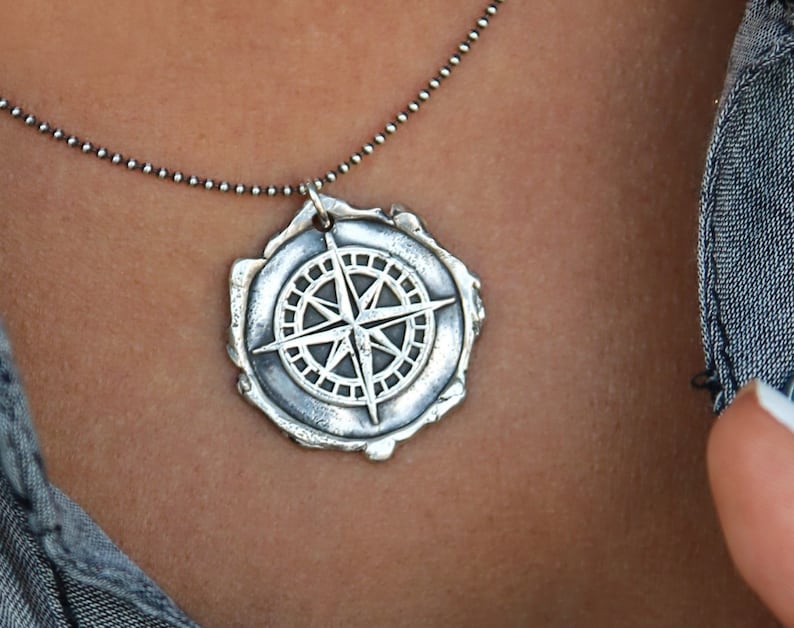 May include: A silver necklace with a compass pendant. The compass is detailed with a star and a circle of points.