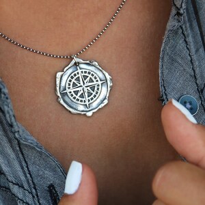 May include: A silver necklace with a compass pendant. The compass is detailed and has a textured, aged look.