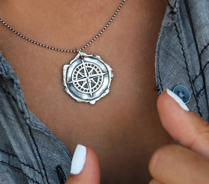 May include: A silver necklace with a compass pendant. The compass is detailed and has a textured, aged look.