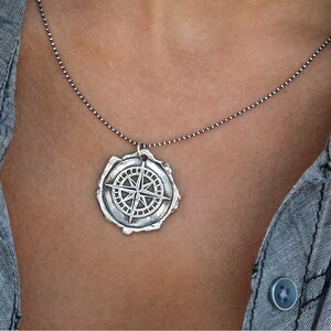 May include: A silver necklace with a compass pendant. The compass is detailed and has a worn, antique look.