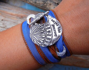 May include: A blue and brown wrap bracelet with a silver charm that says "enjoy the journey".