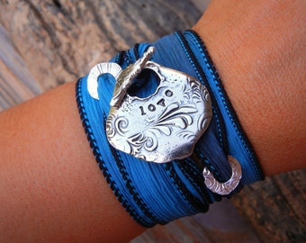 May include: A blue and black fabric bracelet with a silver charm featuring an ornate design and the number "1070" engraved on it.