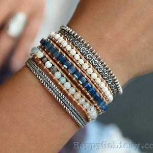 May include: A stack of bracelets with white and blue beads, brown leather, and silver accents.
