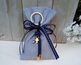 Op de afbeelding: Een klein wit en blauw gestreept stoffen tasje met een gouden ring aan de bovenkant. De tas is vastgebonden met een blauw lint en heeft een gouden bedel met een kruis en een blauwe boze oog.