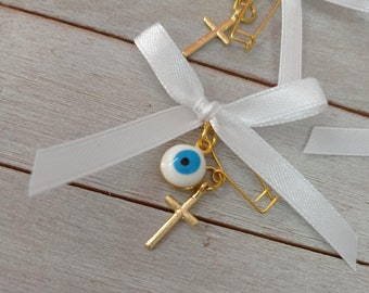 May include: Two white satin ribbons tied with a bow and a safety pin. Each ribbon has a gold cross charm and a blue evil eye charm.