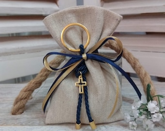 May include: A small, beige linen bag with a gold ring and a blue and gold ribbon. The bag has a gold cross charm with a blue cord attached.