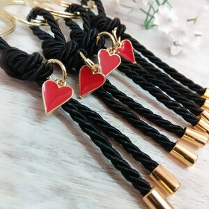 May include: Set of five black rope keychains with gold rings and red heart charms. Each keychain has a gold cap at the end.