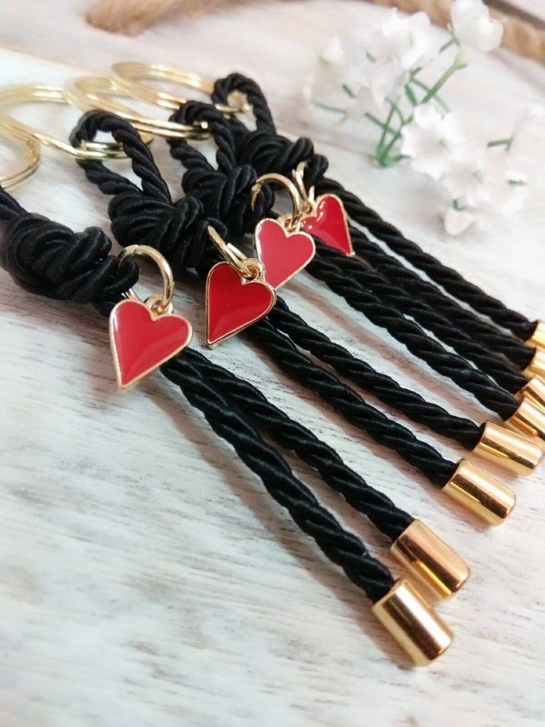 May include: Set of five black rope keychains with gold rings and red heart charms. Each keychain has a gold cap at the end.