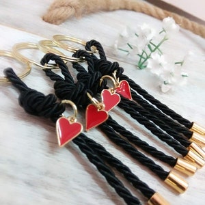 May include: Set of five black rope keychains with gold rings and red heart charms. Each keychain has a gold bead at the end.