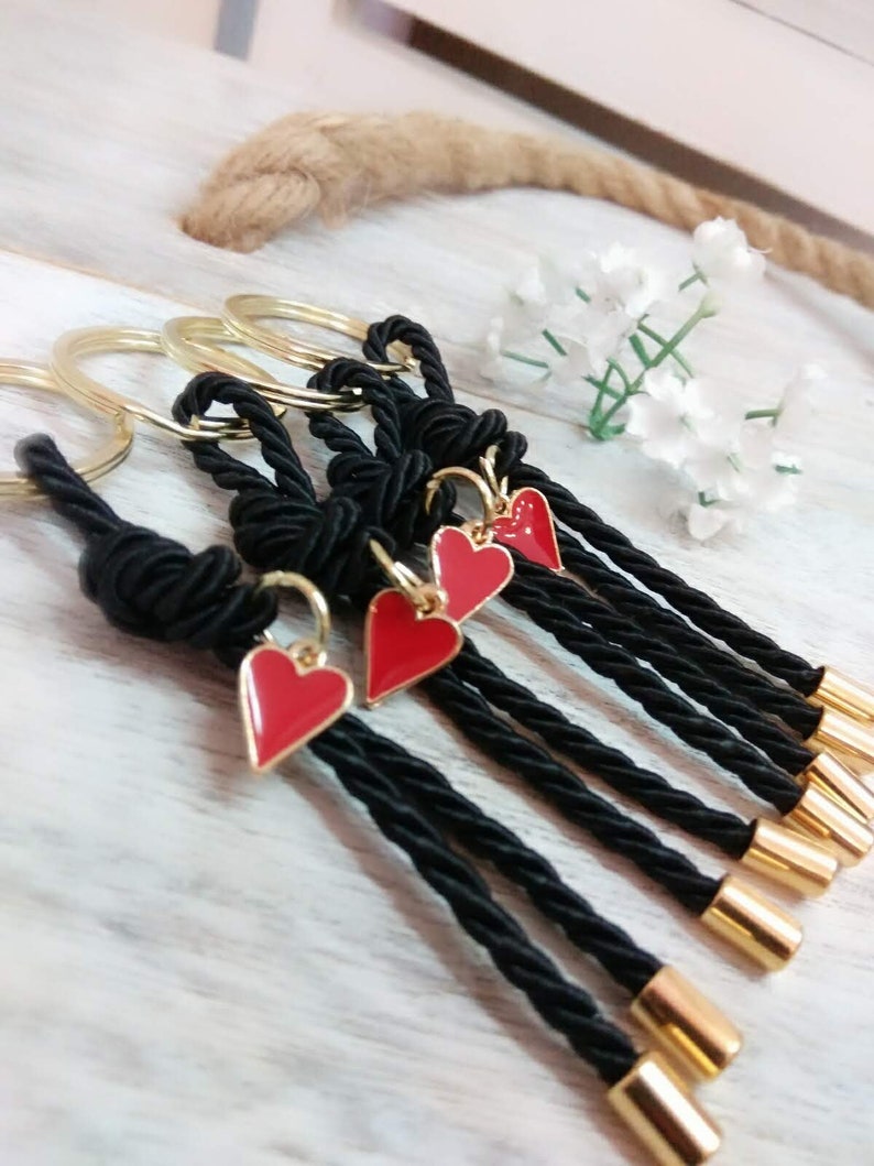 May include: Set of five black rope keychains with gold rings and red heart charms. Each keychain has a gold bead at the end.