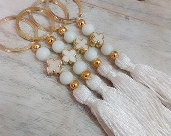 May include: Four gold keychains with white tassel charms. Each keychain features a gold ring, white beads, and gold four-leaf clover charms.