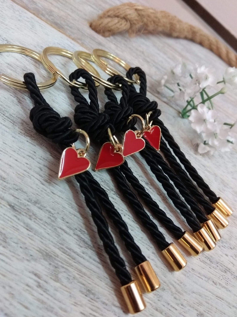May include: Five black keychains with gold rings and red heart charms. Each keychain has a black tassel with a gold tip.
