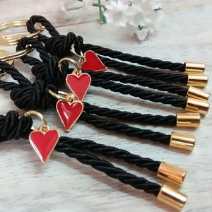 May include: Set of six black rope keychains with gold rings and red heart charms. Each keychain has a gold bead at the end.