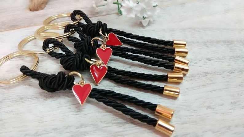 May include: Set of six black rope keychains with gold rings and red heart charms. Each keychain has a gold bead at the end.