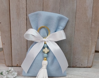 May include: A light blue velvet pouch with a white satin ribbon and a white tassel. The pouch has a gold ring and a beaded charm with a white cross.