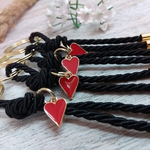 May include: Five black keychains with gold accents and red heart charms. Each keychain has a gold ring and a black braided cord with a gold bead at the end.