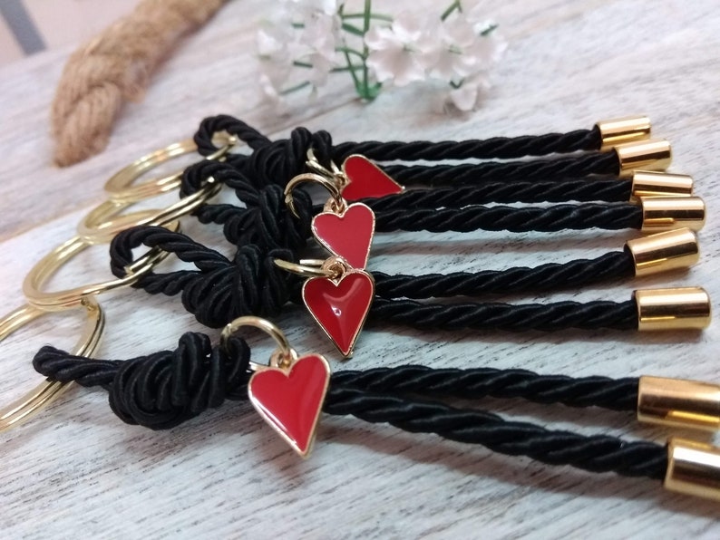 May include: Five black keychains with gold accents and red heart charms. Each keychain has a gold ring and a black braided cord with a gold bead at the end.