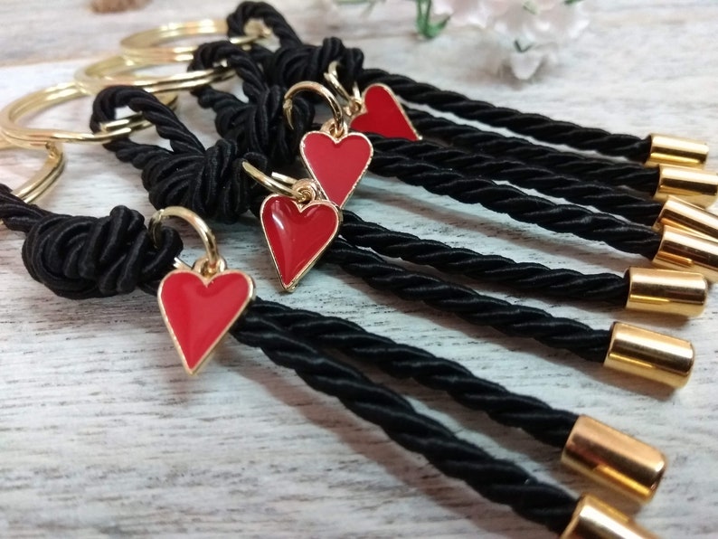 May include: A set of six keychains with black braided cords and gold-toned metal rings. Each keychain features a red heart charm.