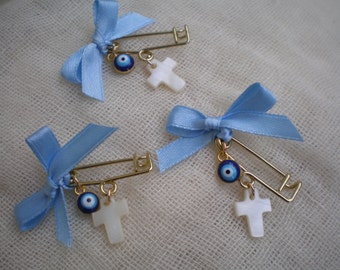 May include: Three blue and white safety pins with blue bows and charms. Each pin has a blue evil eye charm and a white cross charm.