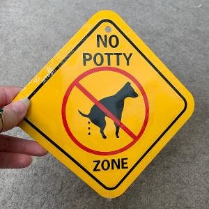 May include: Yellow diamond-shaped sign with a red circle and a diagonal line through it. The sign says "NO POTTY ZONE" and depicts a black silhouette of a dog relieving itself.