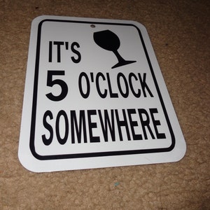 May include: White metal sign with black text and a black wine glass silhouette. The sign reads "It's 5 O'Clock Somewhere".