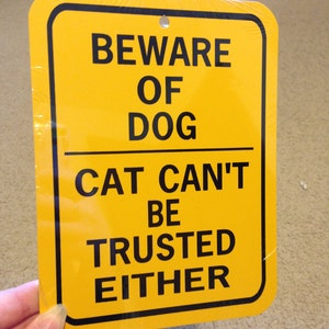 May include: Yellow metal sign with black text that reads "Beware of Dog Cat Can't Be Trusted Either".