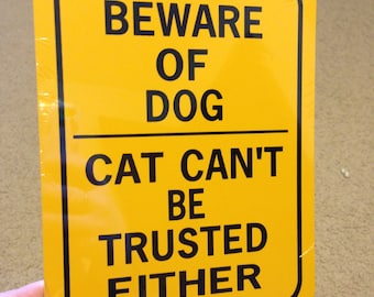 Puede incluir: Señal de metal amarilla con texto negro que dice "Cuidado con el perro El gato no se puede confiar tampoco".