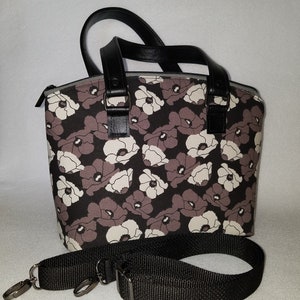 May include: A black and white floral print tote bag with black leather handles and a detachable black strap. The bag has a zipper closure.