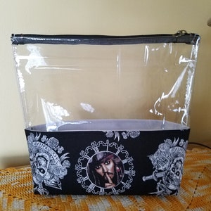 May include: Clear plastic zippered pouch with a black fabric lining featuring a repeated pattern of a clock face with a pirate character inside and a skull and crossbones design.
